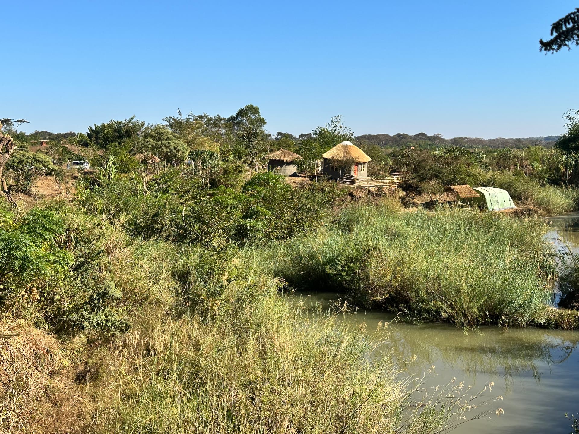 The project land near Lilongwe: a river bordered by tall grass, with thatched buildings among the trees